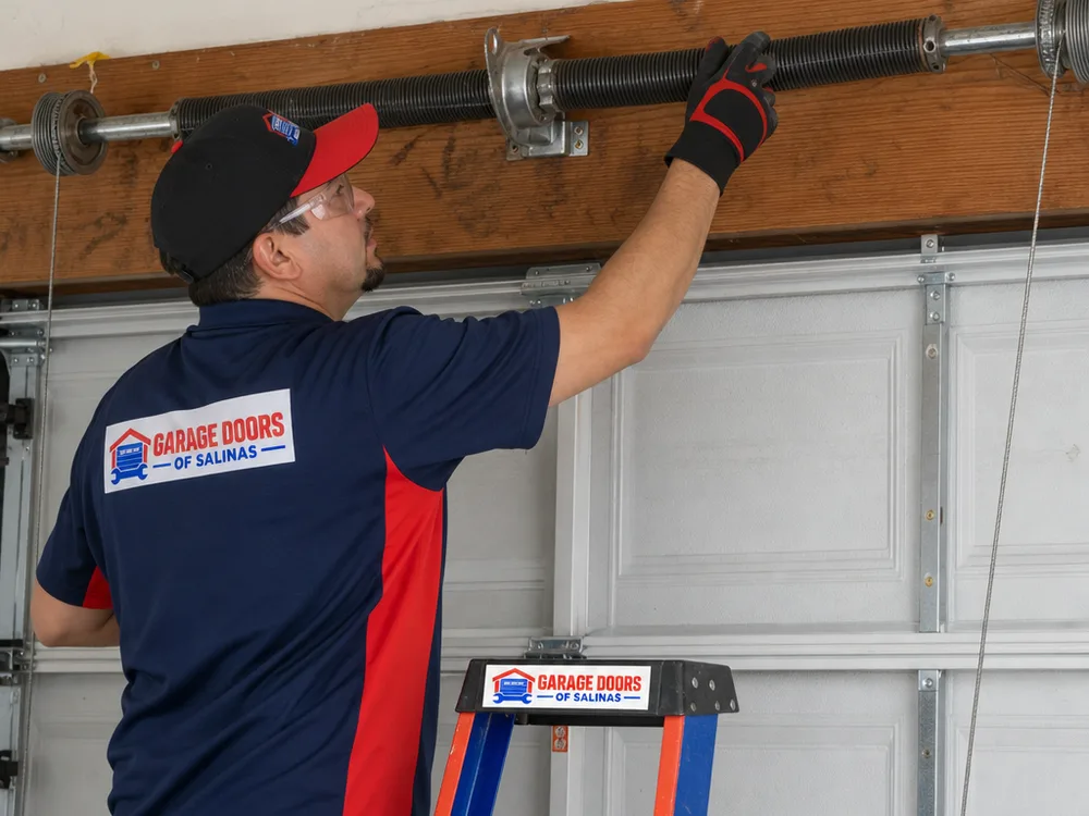 Contractor inspecting a garage door torsion spring assembly, center bearing plate, cables and brackets