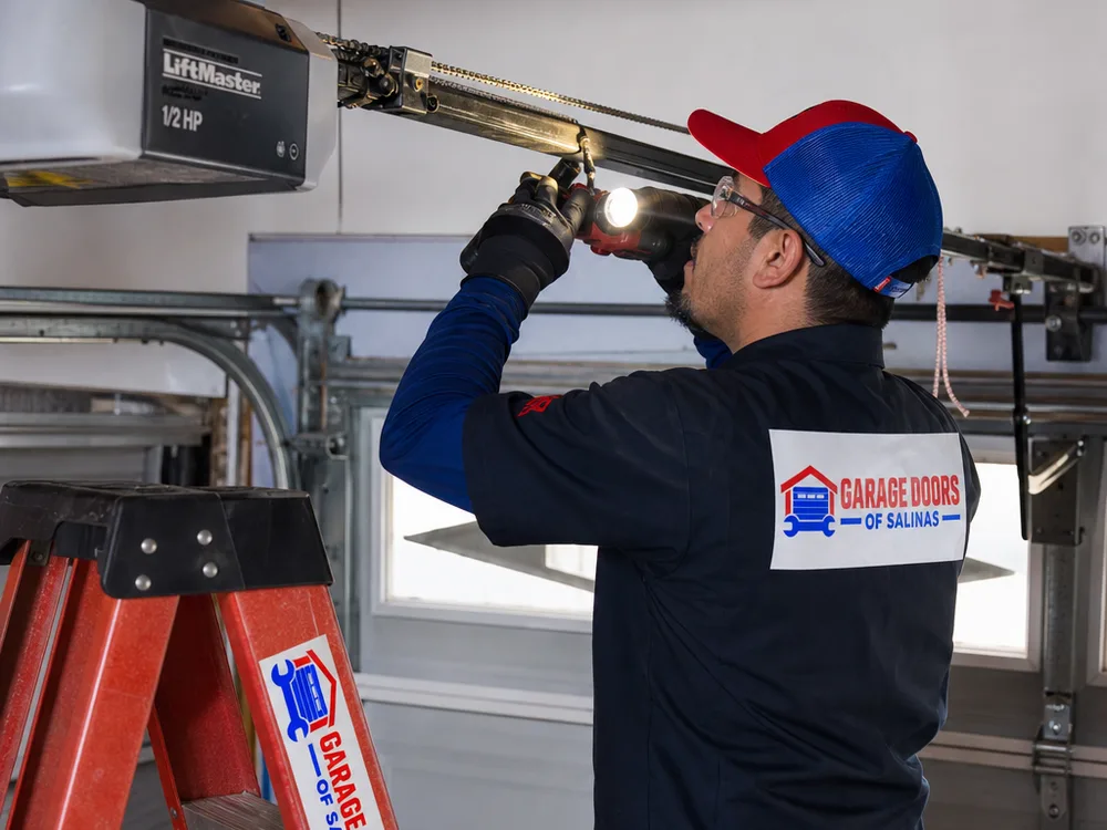 Contractor inspecting a garage door opener rail, drive system, and trolley connection above the door